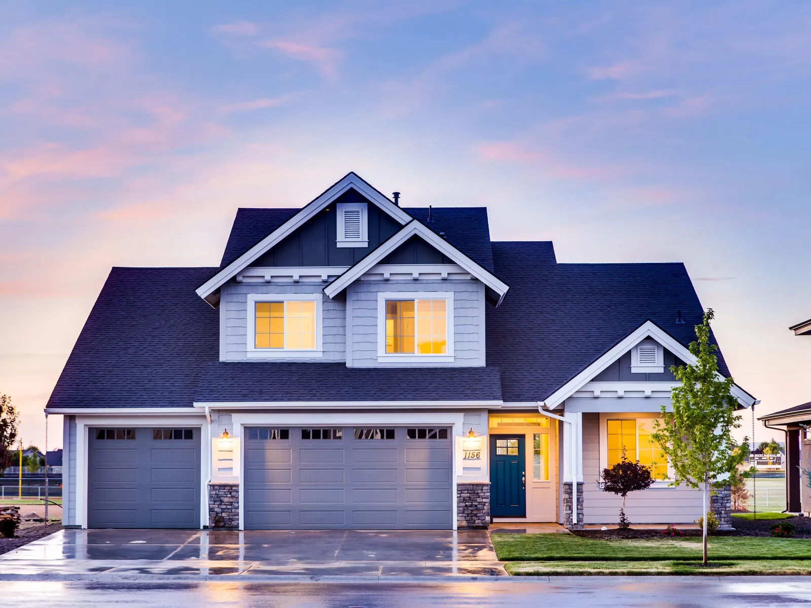 A two-story house with a double garage door at dusk.